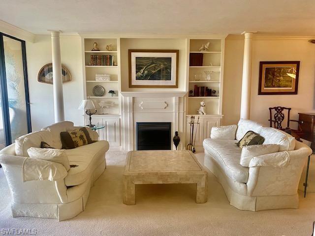 Living room with crown molding, built in features, light colored carpet, and decorative columns