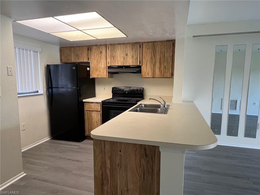 Kitchen with black appliances, light countertops, brown cabinetry, a peninsula, and wood finished floors