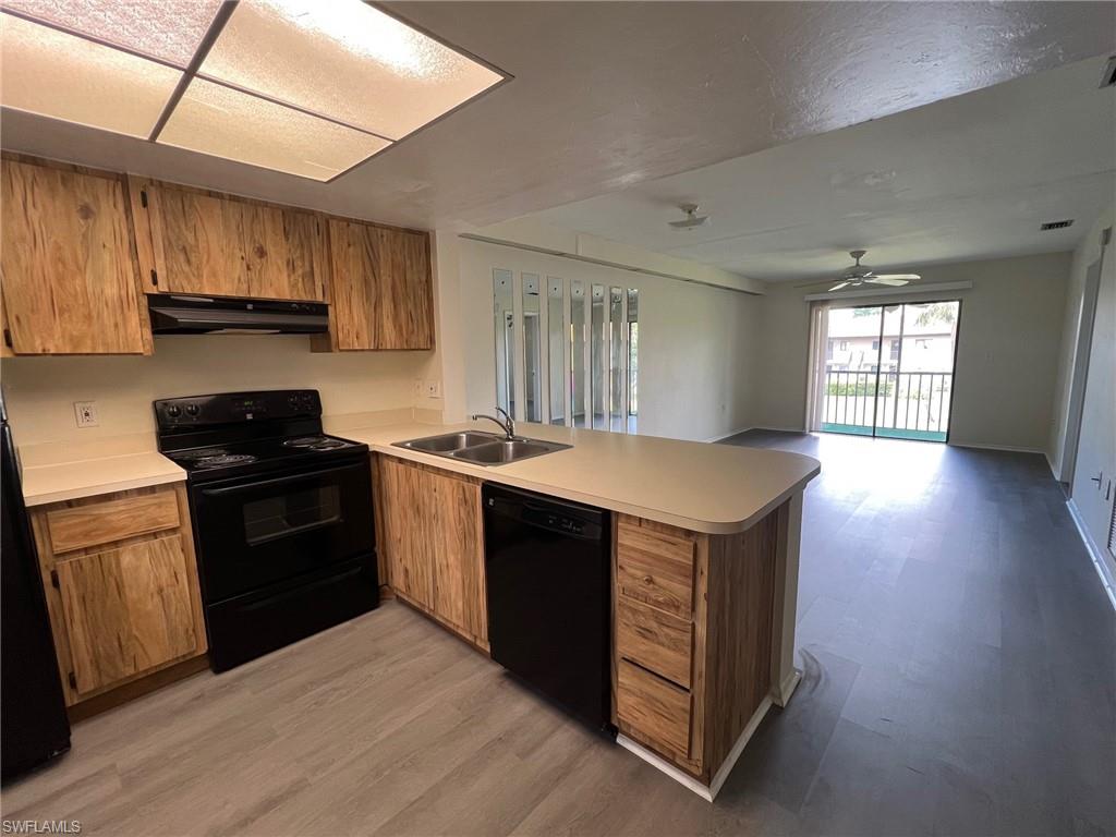 Kitchen featuring black appliances, a peninsula, brown cabinets, light wood-style floors, and light countertops