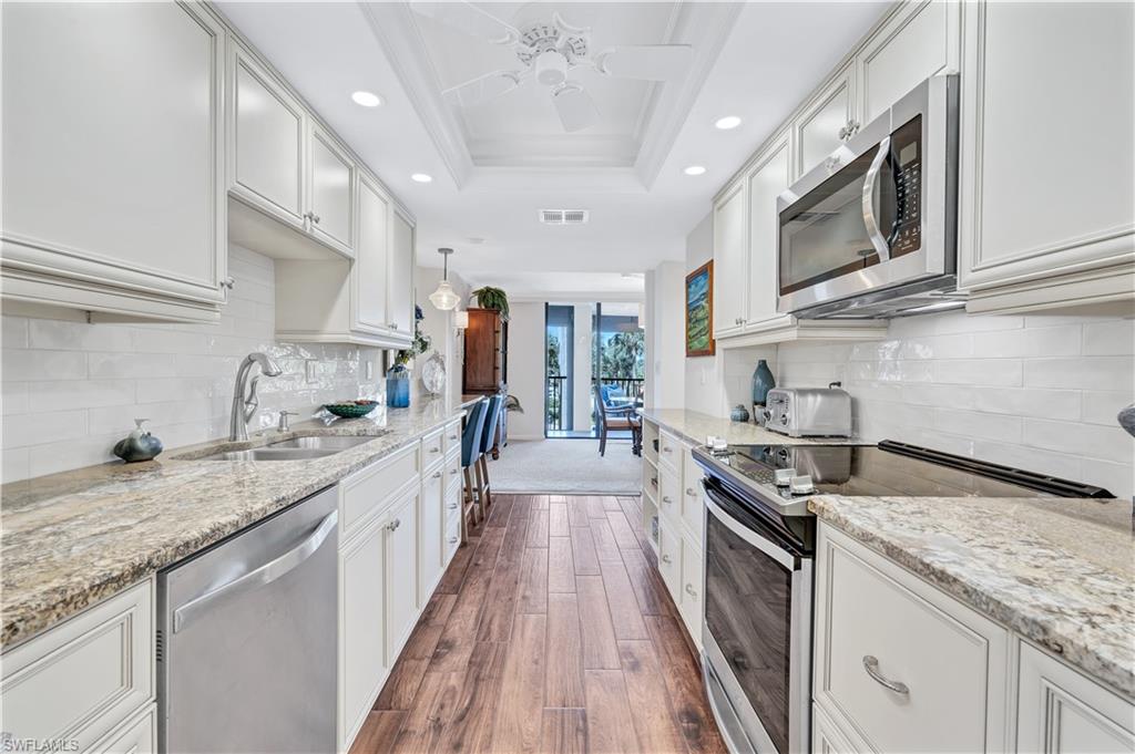 Kitchen with stainless steel appliances, recessed lighting, dark wood finished floors, ornamental molding, and light stone counters
