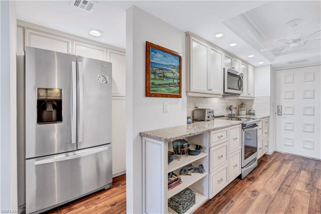 Kitchen featuring appliances with stainless steel finishes, decorative backsplash, wood finished floors, recessed lighting, and light stone counters