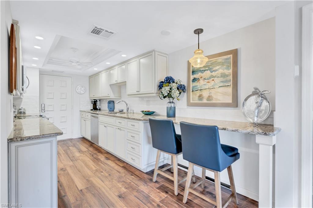 Kitchen featuring tasteful backsplash, light wood-type flooring, light stone countertops, white cabinetry, and recessed lighting