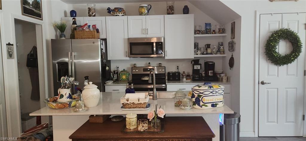 Kitchen featuring stainless steel appliances, white cabinets, light stone countertops, and a kitchen island with sink