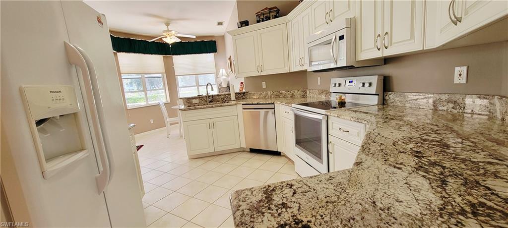 Kitchen with white appliances, light tile patterned floors, light stone counters, a ceiling fan, and a peninsula
