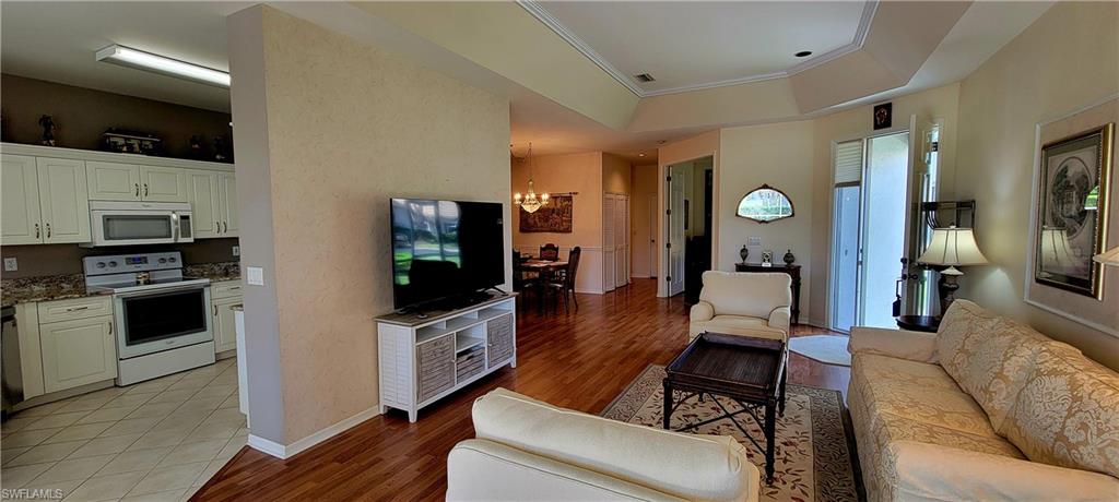 Living area featuring a chandelier, light wood-type flooring, a raised ceiling, and ornamental molding
