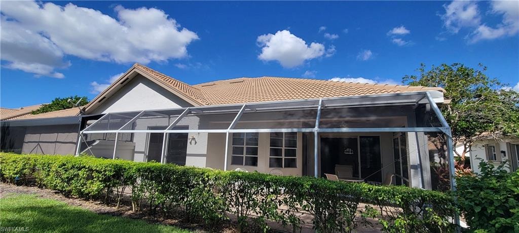 Rear view of house with enclosure, a tile roof, a sunroom, and stucco siding