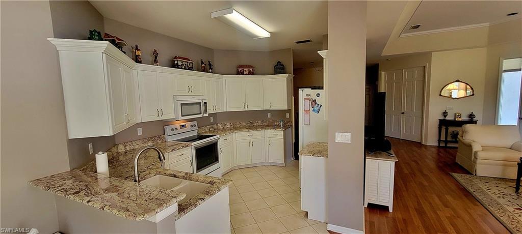Kitchen with white appliances, open floor plan, white cabinetry, light stone counters, and a peninsula