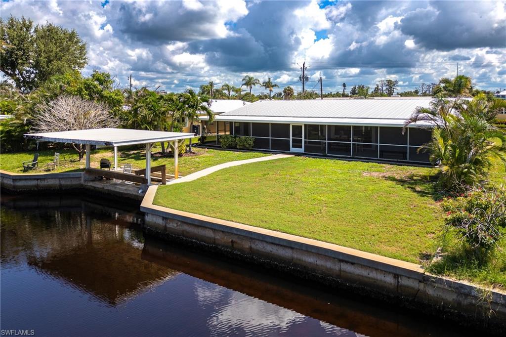 Back of property with screened lanai, metal roof, covered boathouse, concrete seawall, and plenty of yard space for a pool.
