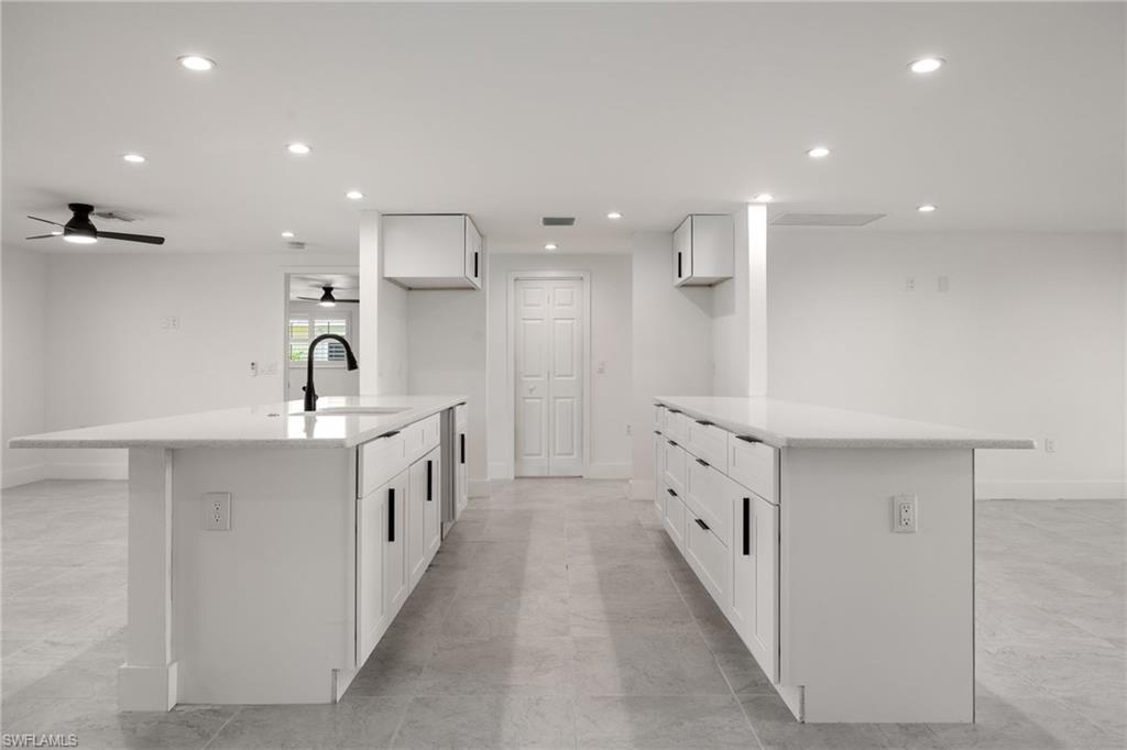 Sleek kitchen with dual peninsulas, light stone countertops, recessed lighting, breakfast bar seating, and modern white cabinetry.