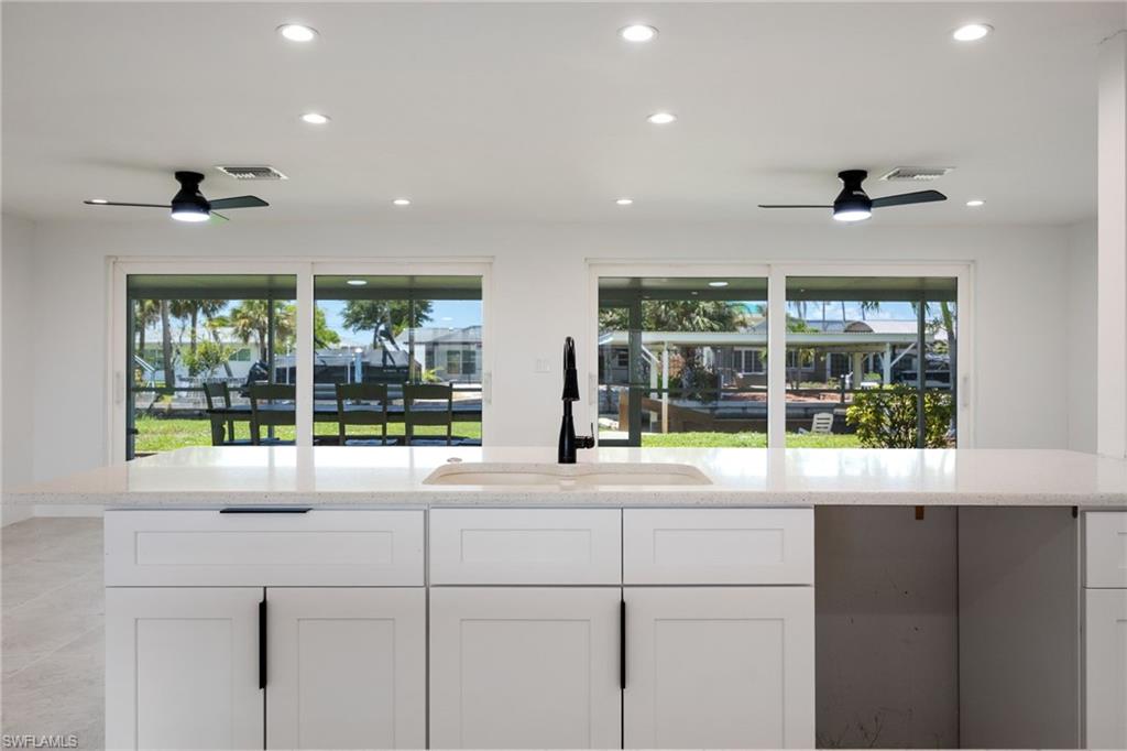 Kitchen with recessed lighting, light stone countertops, white cabinetry, and expansive windows showcasing waterfront views.