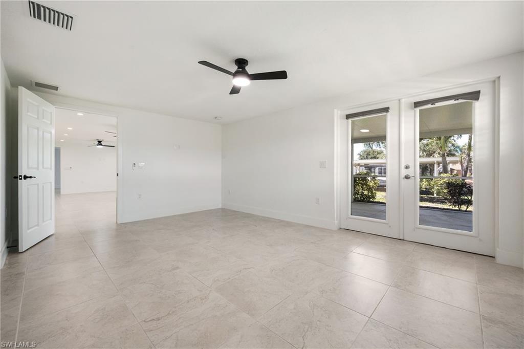 Spacious master bedroom with French doors to the outdoors, neutral tile flooring, and ceiling fan.