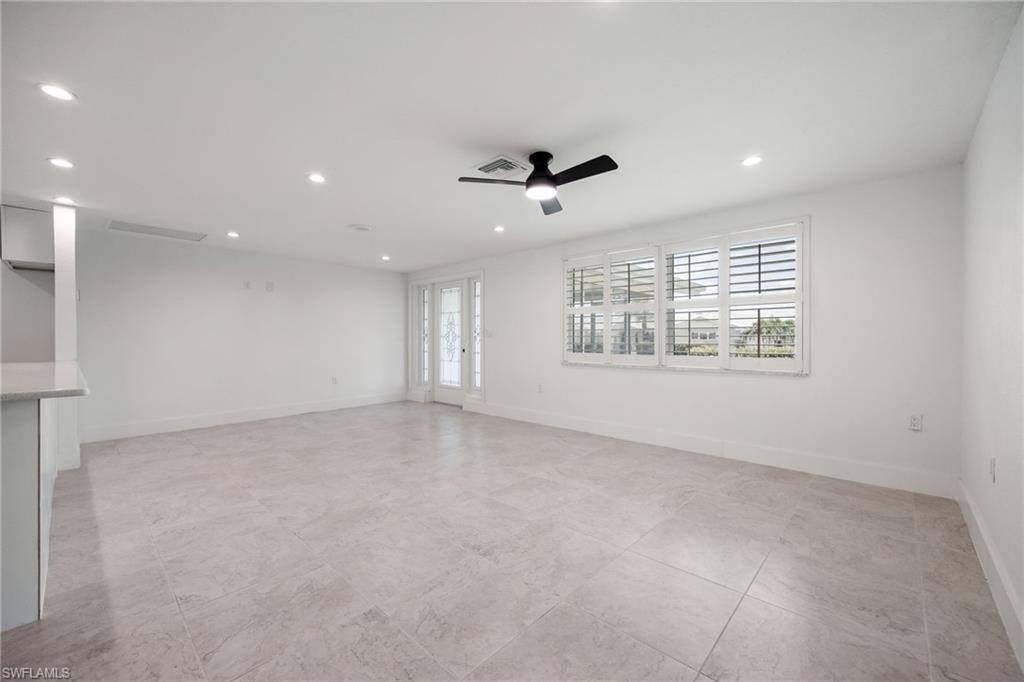 Light-filled living area with neutral tile flooring, plantation shutters, and access to the front entry