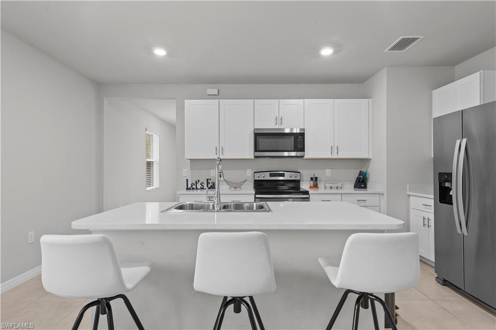 Kitchen with appliances with stainless steel finishes, a breakfast bar, light tile patterned floors, white cabinets, and recessed lighting