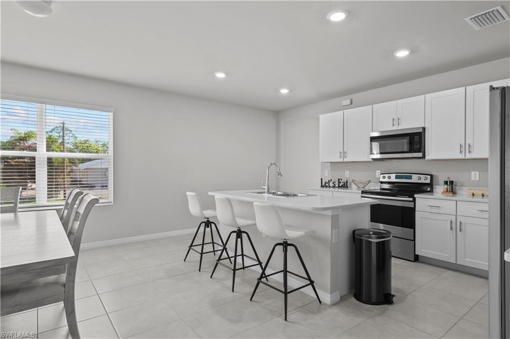 Kitchen featuring stainless steel appliances, a kitchen island with sink, a kitchen breakfast bar, light countertops, and white cabinetry