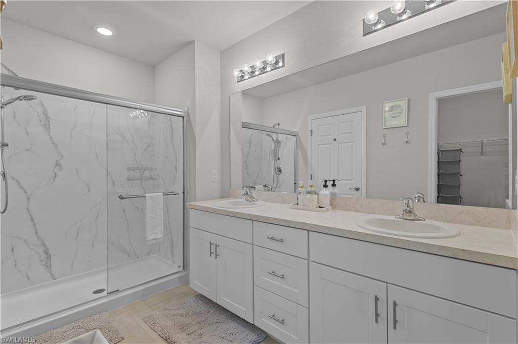 Full bath with a marble finish shower, double vanity, a walk in closet, tile patterned floors, and recessed lighting