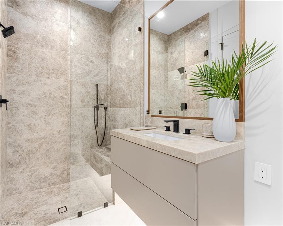 Bathroom featuring vanity, walk in shower, marble slab walls, bench and hand shower