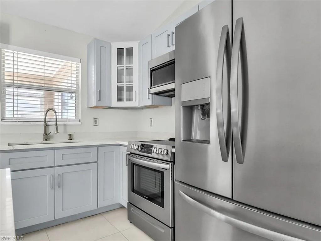 Kitchen with appliances with stainless steel finishes, glass insert cabinets, light countertops, and light tile patterned floors