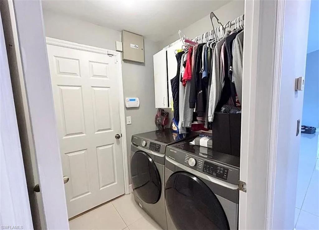 Washroom with cabinet space, washing machine and clothes dryer, and light tile patterned floors