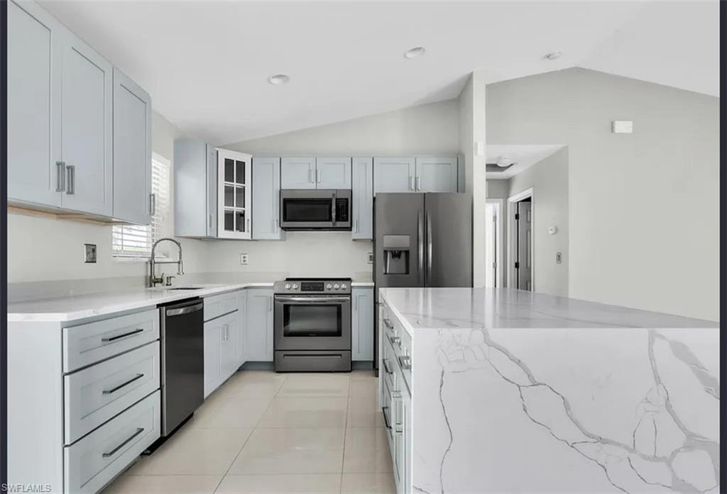 Kitchen with lofted ceiling, appliances with stainless steel finishes, light stone countertops, glass insert cabinets, and light tile patterned floors