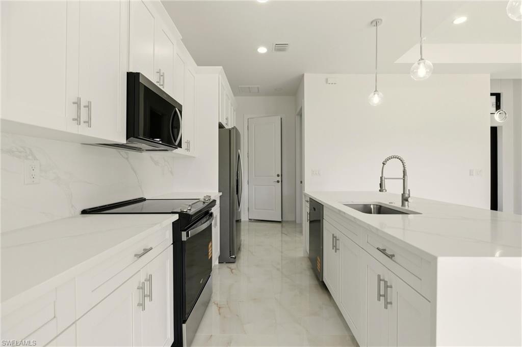 Kitchen with appliances with stainless steel finishes, white cabinetry, pendant lighting, light stone countertops, and recessed lighting