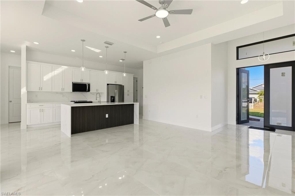 Kitchen featuring pendant lighting, white cabinetry, a center island with sink, open floor plan, and stainless steel appliances