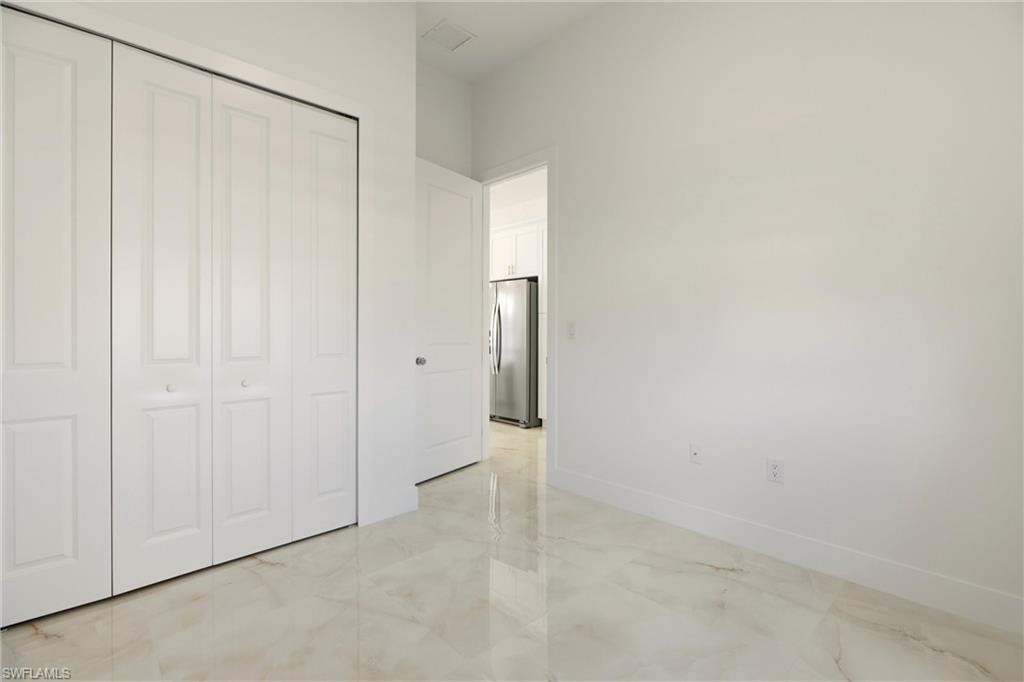 Unfurnished bedroom with freestanding refrigerator, light marble finish floors, and a closet