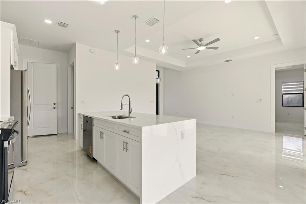 Kitchen with white cabinets, light stone countertops, hanging light fixtures, recessed lighting, and a raised ceiling