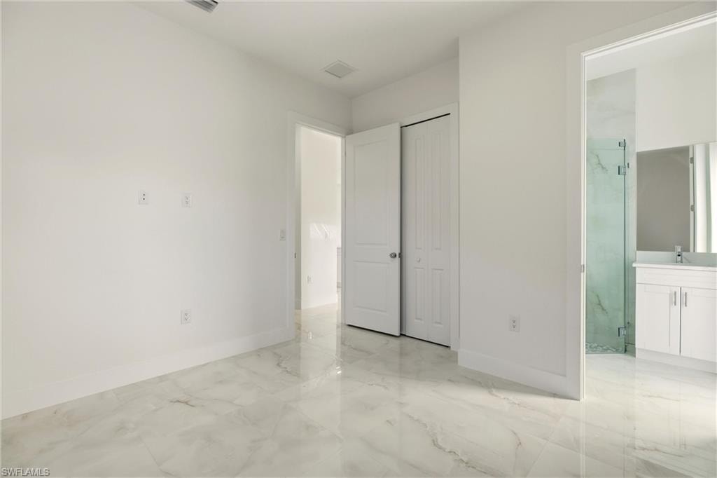 Unfurnished bedroom featuring connected bathroom, light marble finish flooring, and a closet