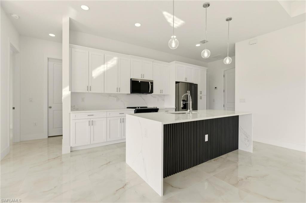 Kitchen with hanging light fixtures, white cabinetry, stainless steel appliances, light stone countertops, and decorative backsplash