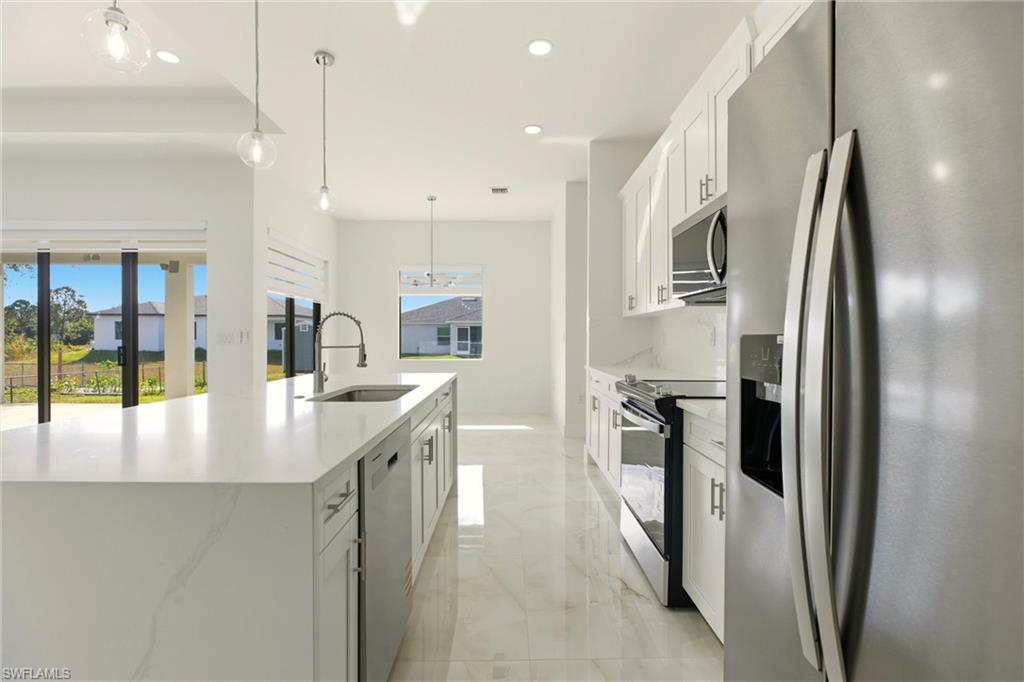Kitchen with appliances with stainless steel finishes, white cabinetry, decorative light fixtures, light stone countertops, and a large island