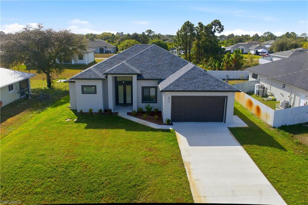 French country style house featuring stucco siding, driveway, roof with shingles, an attached garage, and a residential view