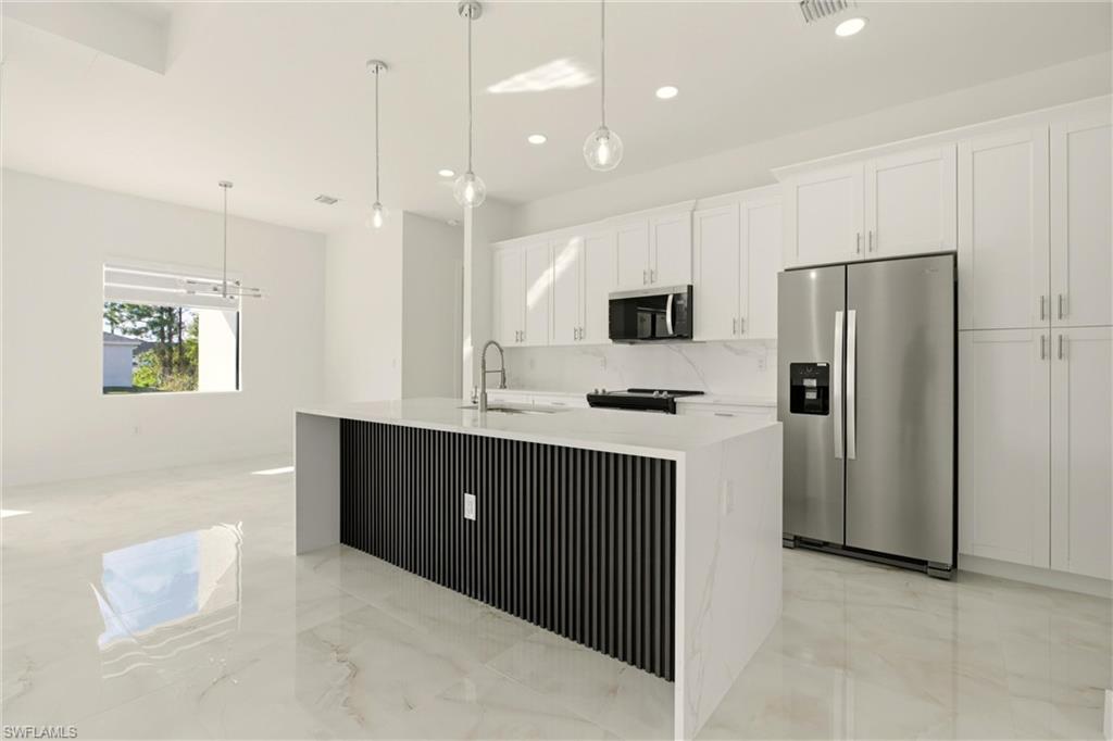 Kitchen with appliances with stainless steel finishes, hanging light fixtures, recessed lighting, white cabinets, and light stone countertops