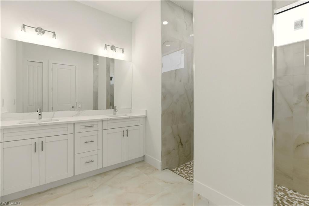 Bathroom with double vanity, a marble finish shower, and light marble finish floors