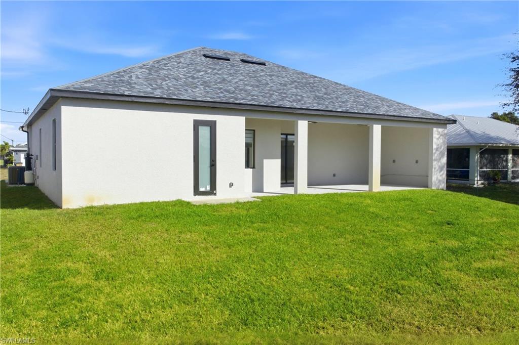 Rear view of house featuring a shingled roof, a yard, a patio, and stucco siding