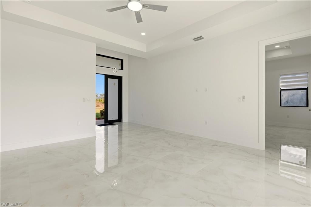 Empty room featuring a raised ceiling, light marble finish flooring, recessed lighting, and ceiling fan