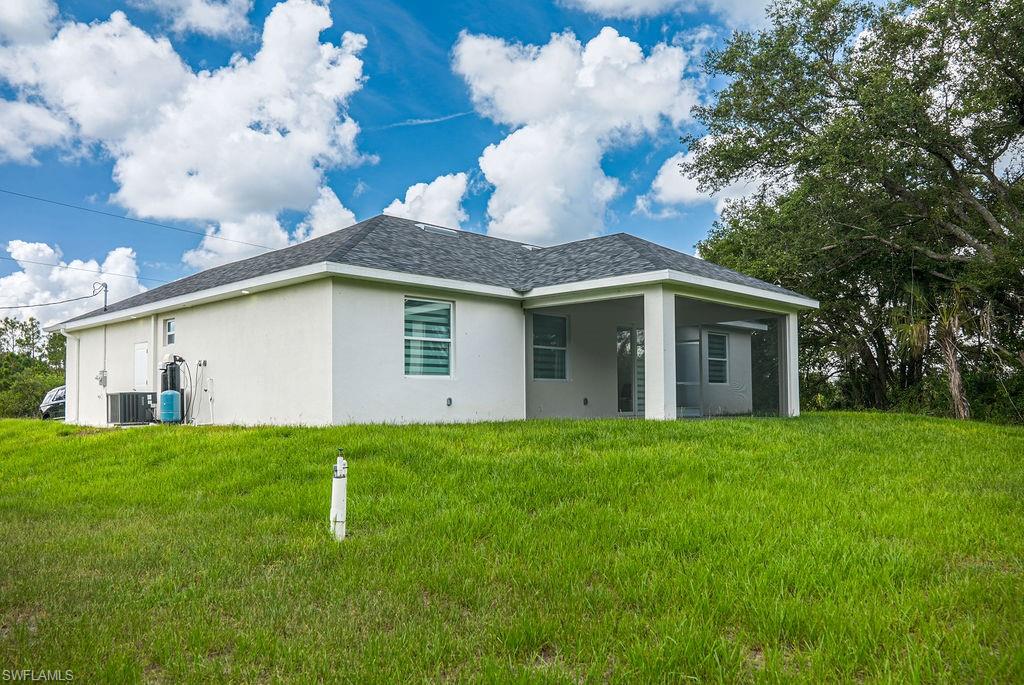 Back of house with stucco siding, a lawn, and roof with shingles