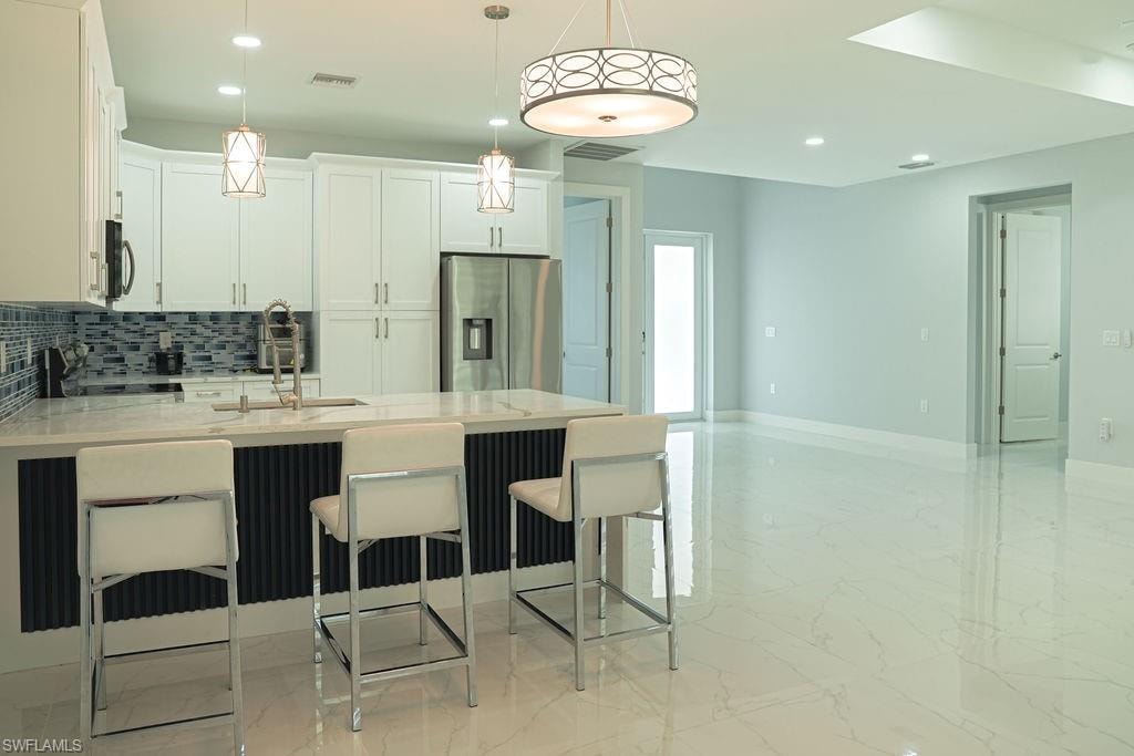 Kitchen featuring light marble finish floors, tasteful backsplash, stainless steel fridge, recessed lighting, and a peninsula