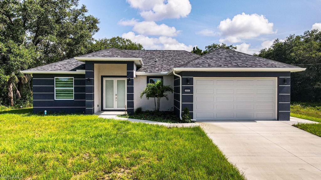 View of front of house featuring a garage, driveway, a front yard, stucco siding, and a shingled roof