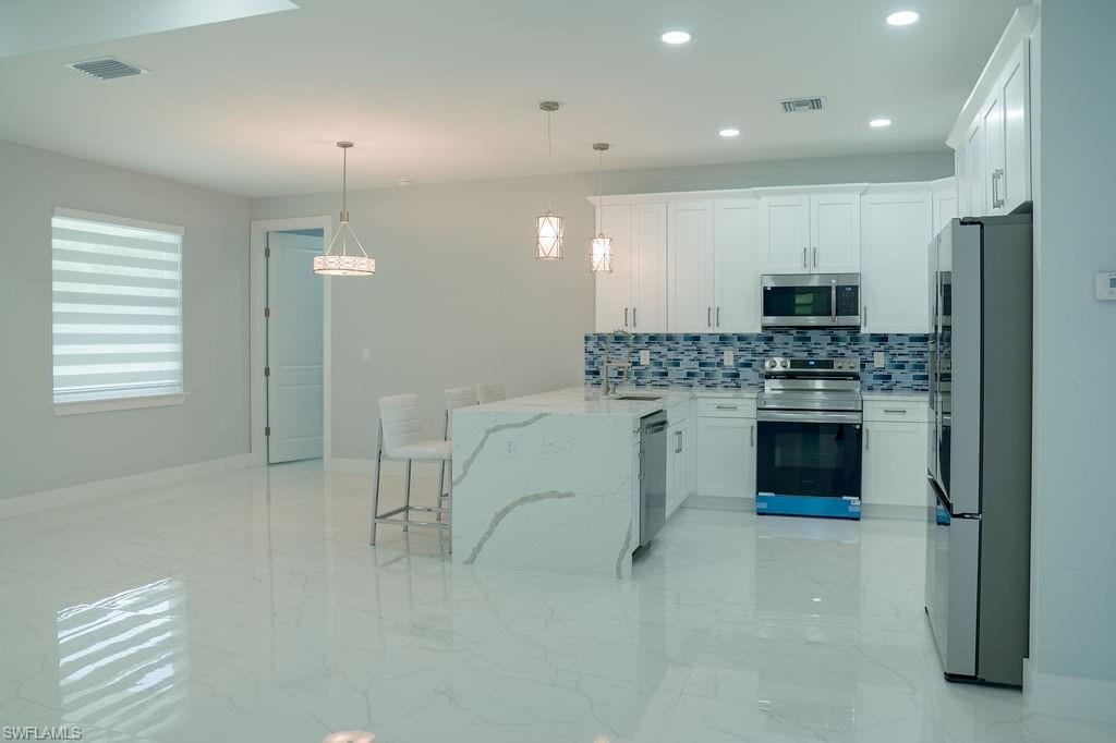 Kitchen with appliances with stainless steel finishes, light marble finish flooring, decorative backsplash, a peninsula, and white cabinets