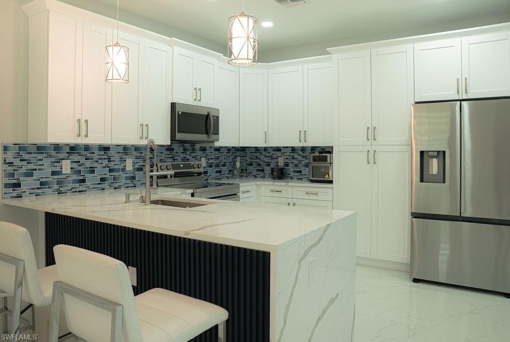 Kitchen featuring stainless steel appliances, a peninsula, light stone countertops, decorative backsplash, and light marble finish floors