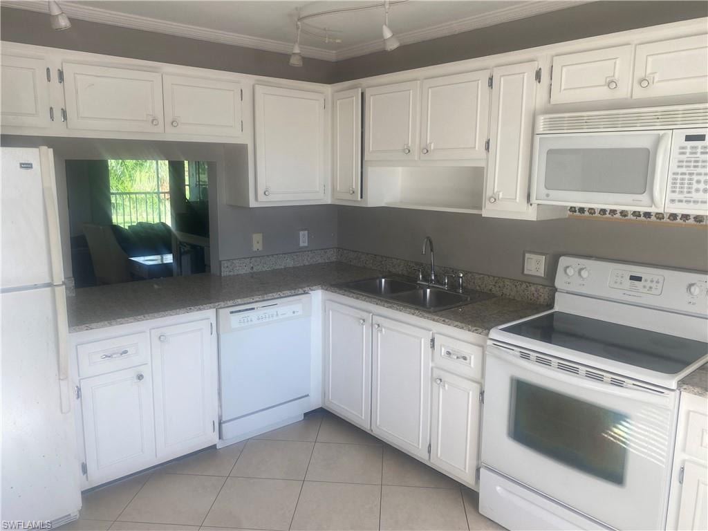 Kitchen with white appliances, white cabinetry, light tile patterned flooring, and crown molding