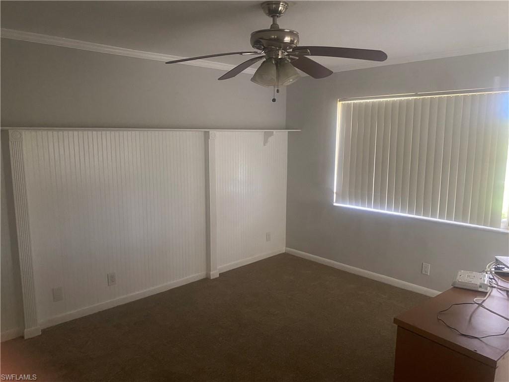 Spare room with a ceiling fan, dark carpet, and ornamental molding