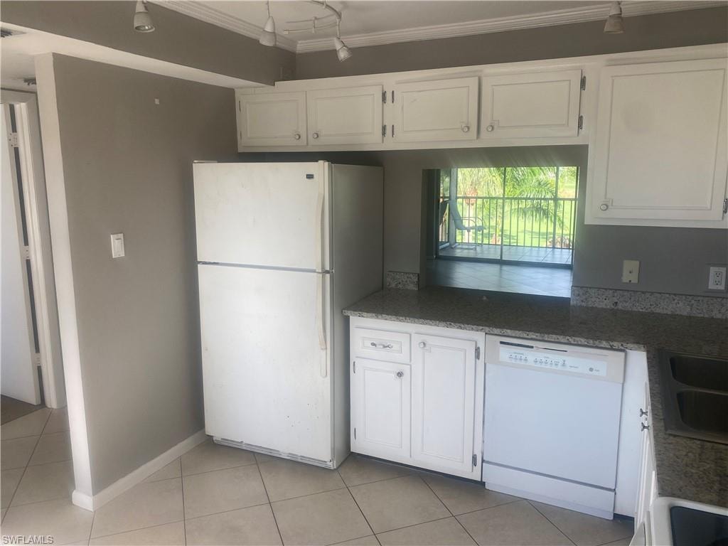 Kitchen with white appliances, white cabinetry, light tile patterned flooring, ornamental molding, and dark stone countertops