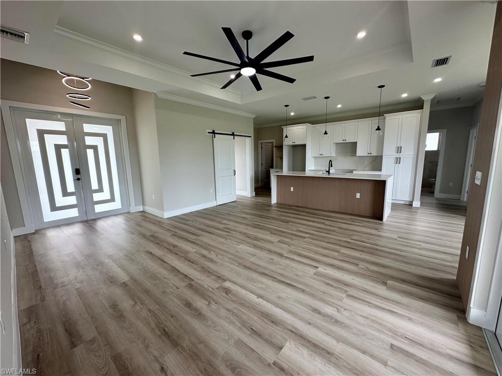 Living area with a tray ceiling, a barn door, light wood-type flooring, ornamental molding, and recessed lighting. Pictures virtually staged for illustrative purposes only