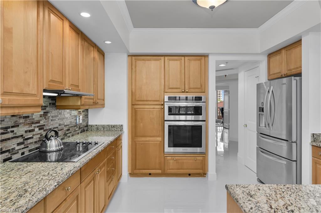 Kitchen with tasteful backsplash, appliances with stainless steel finishes, recessed lighting, ornamental molding, and light stone counters