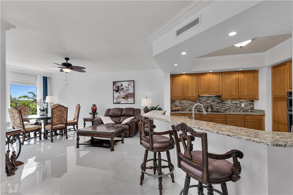 Kitchen with crown molding, tasteful backsplash, light stone countertops, a breakfast bar area, and brown cabinets