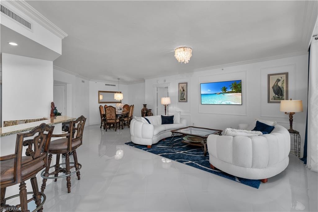 Tiled living room with crown molding, a chandelier, and a decorative wall