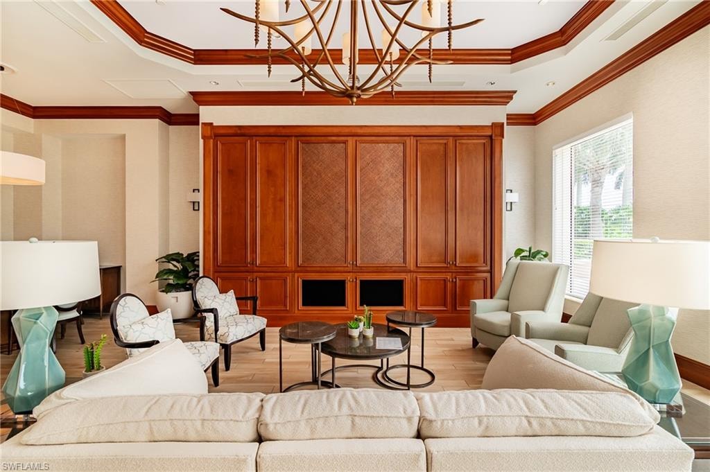 Living room with light wood finished floors, a raised ceiling, ornamental molding, and a chandelier