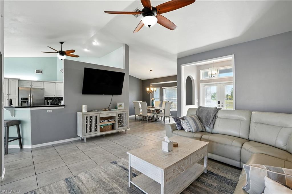 Living room with a ceiling fan, light tile patterned floors, a chandelier, and high vaulted ceiling