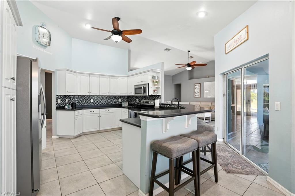 Kitchen with high vaulted ceiling, a ceiling fan, a kitchen breakfast bar, appliances with stainless steel finishes, and a peninsula